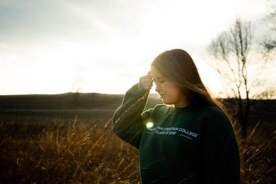 During the day, a woman wearing a black hoodie stood at brown grass
